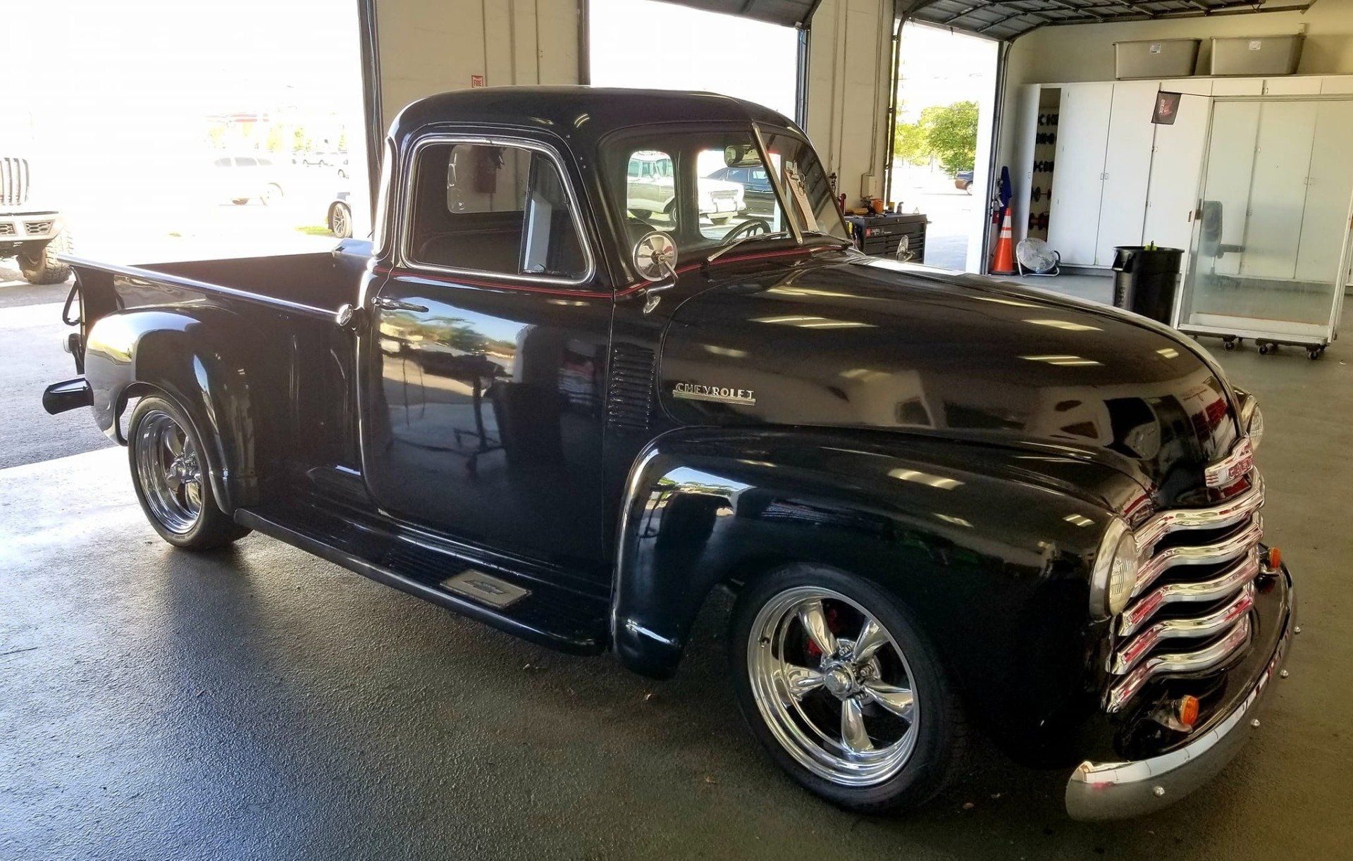 Black vintage Chevrolet pickup truck parked in a garage with shiny chrome wheels and grille.