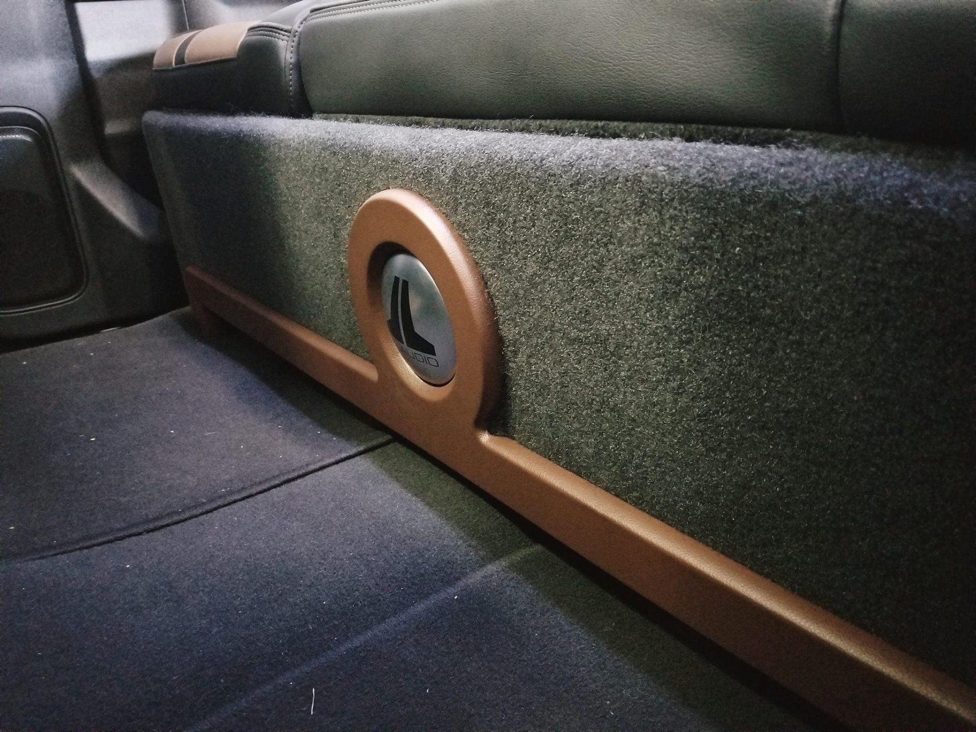 Custom car subwoofer enclosure, brown trim, black speaker grill, installed under a seat.