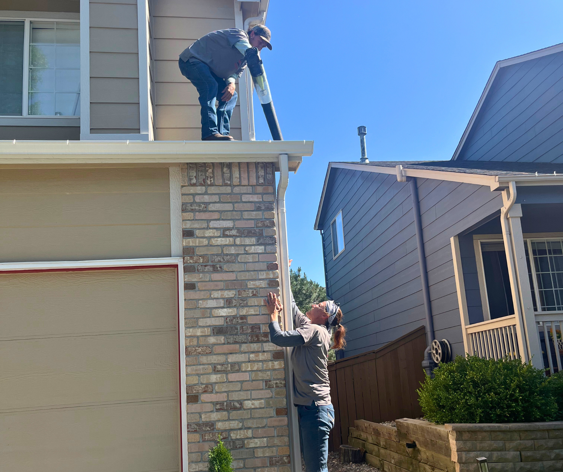 A man in a red shirt and blue hat is working on a roof.
