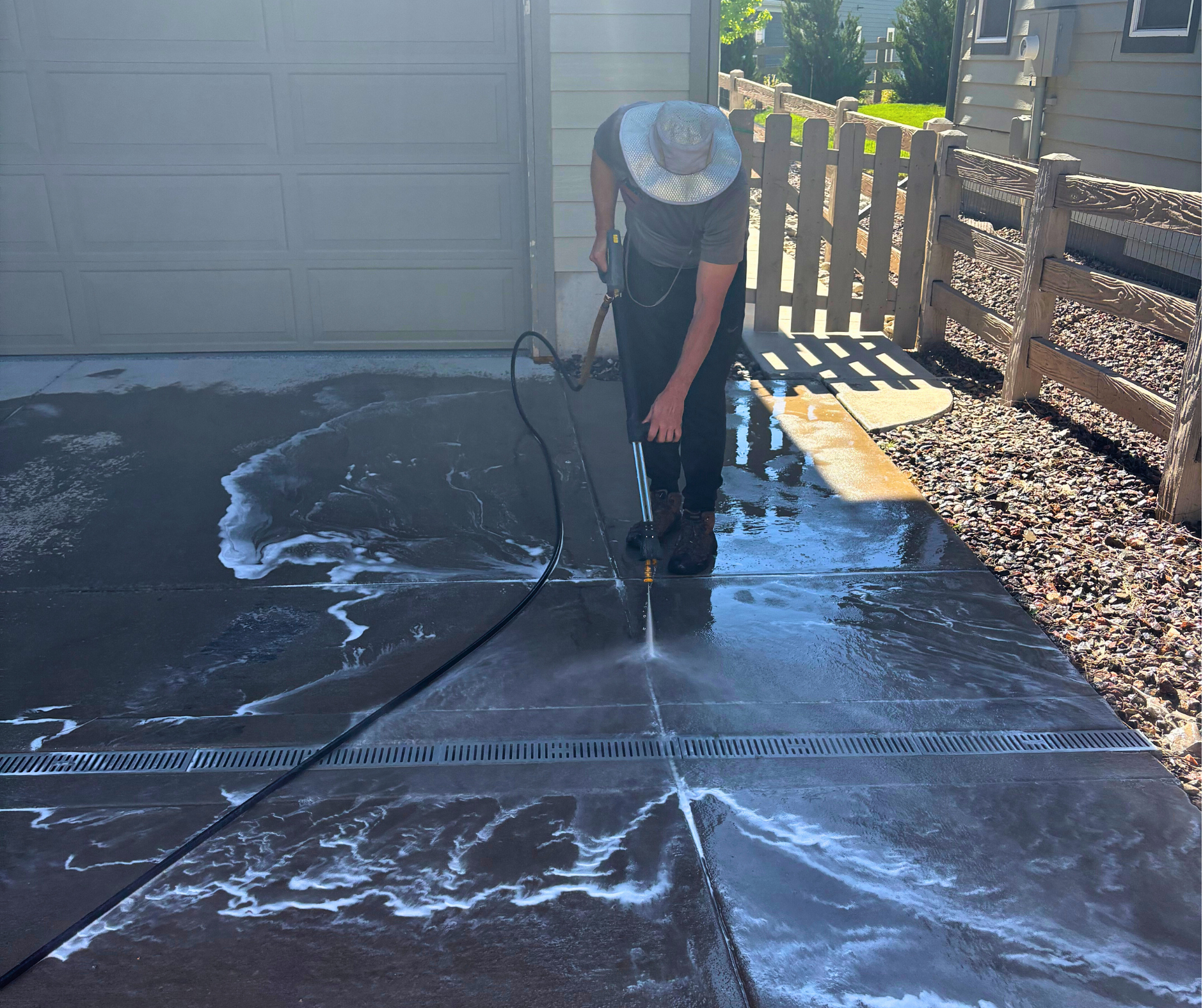 A man is using a pressure washer to clean the sidewalk in front of a house.