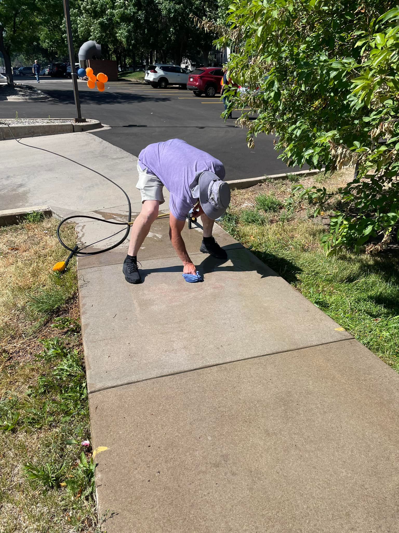 A man is bending over to clean a sidewalk with a hose.