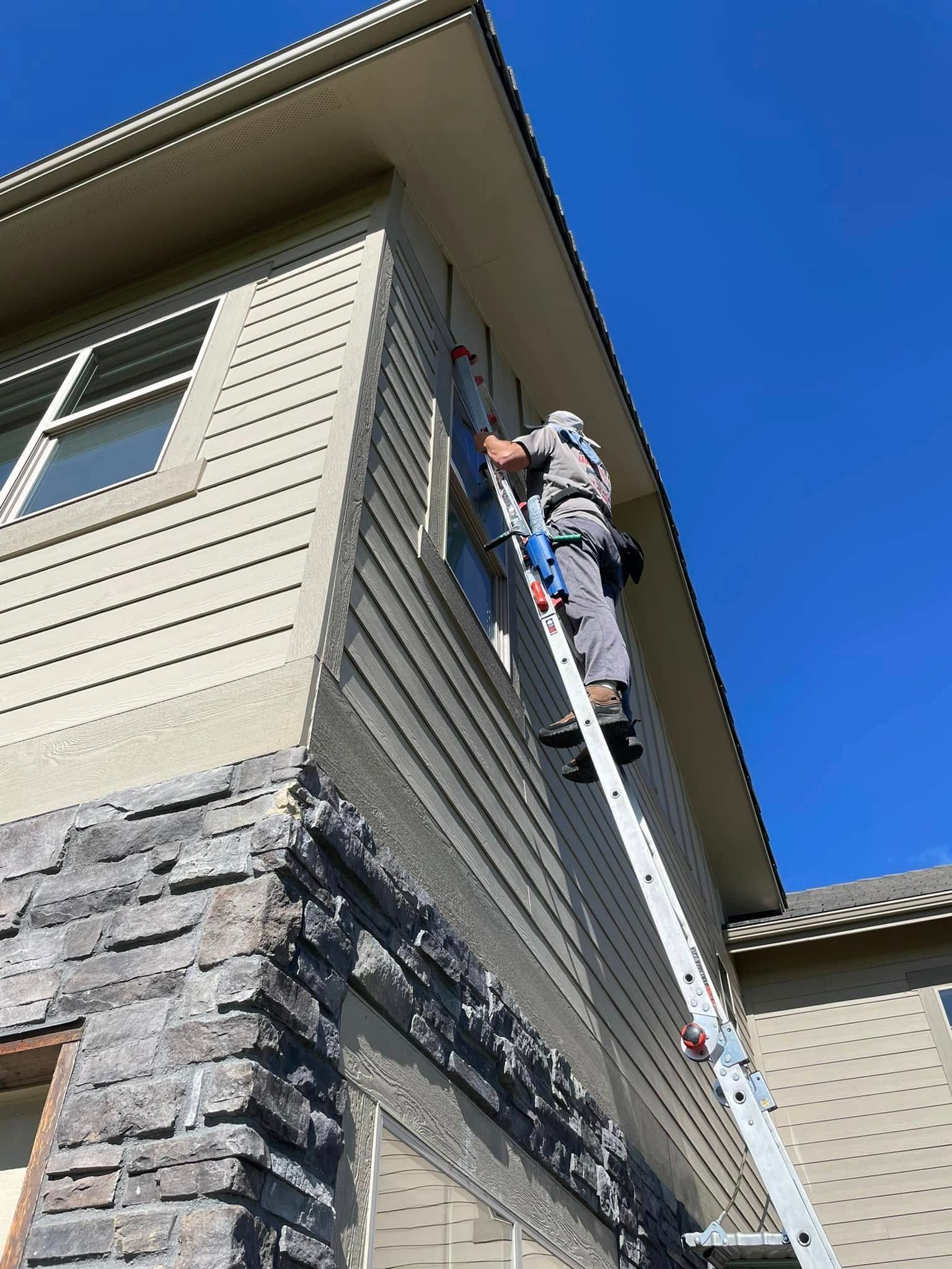 A man is standing on a ladder on the side of a house.