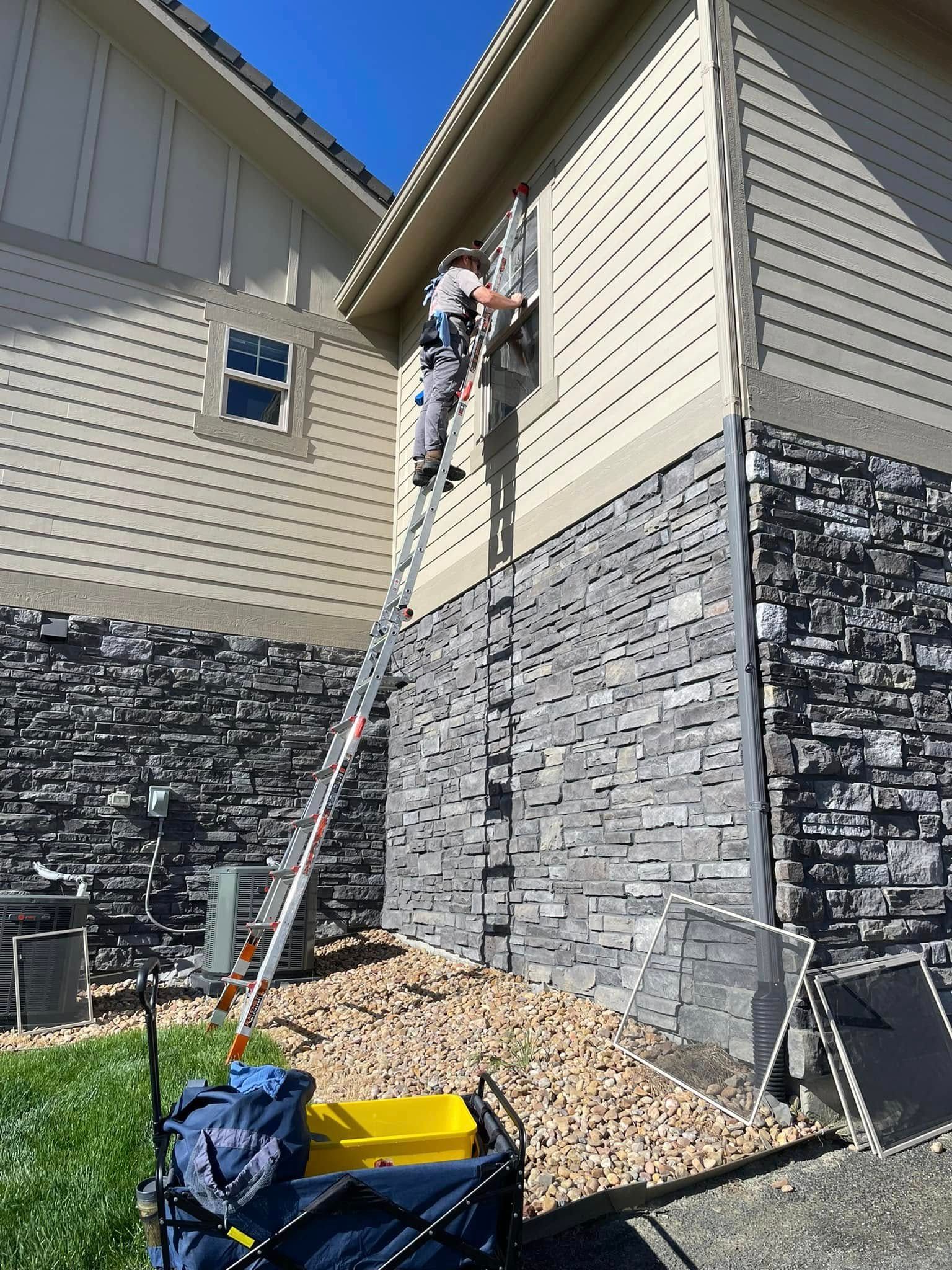 A man on a ladder is painting the side of a house.
