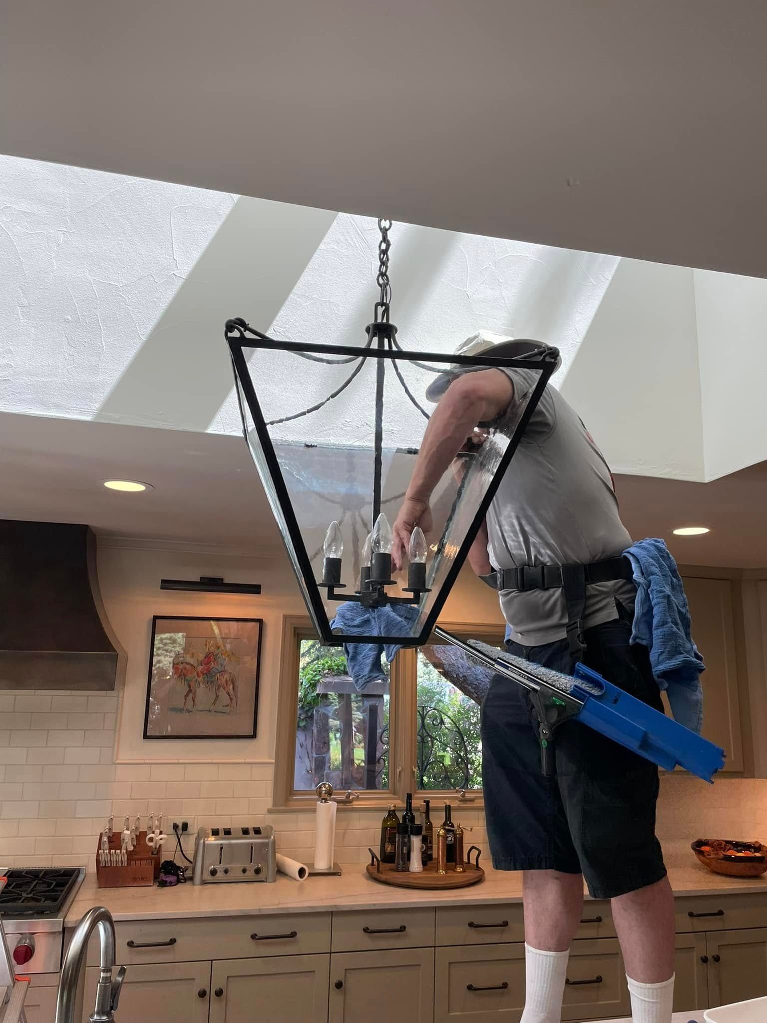 A man is cleaning a chandelier in a kitchen.