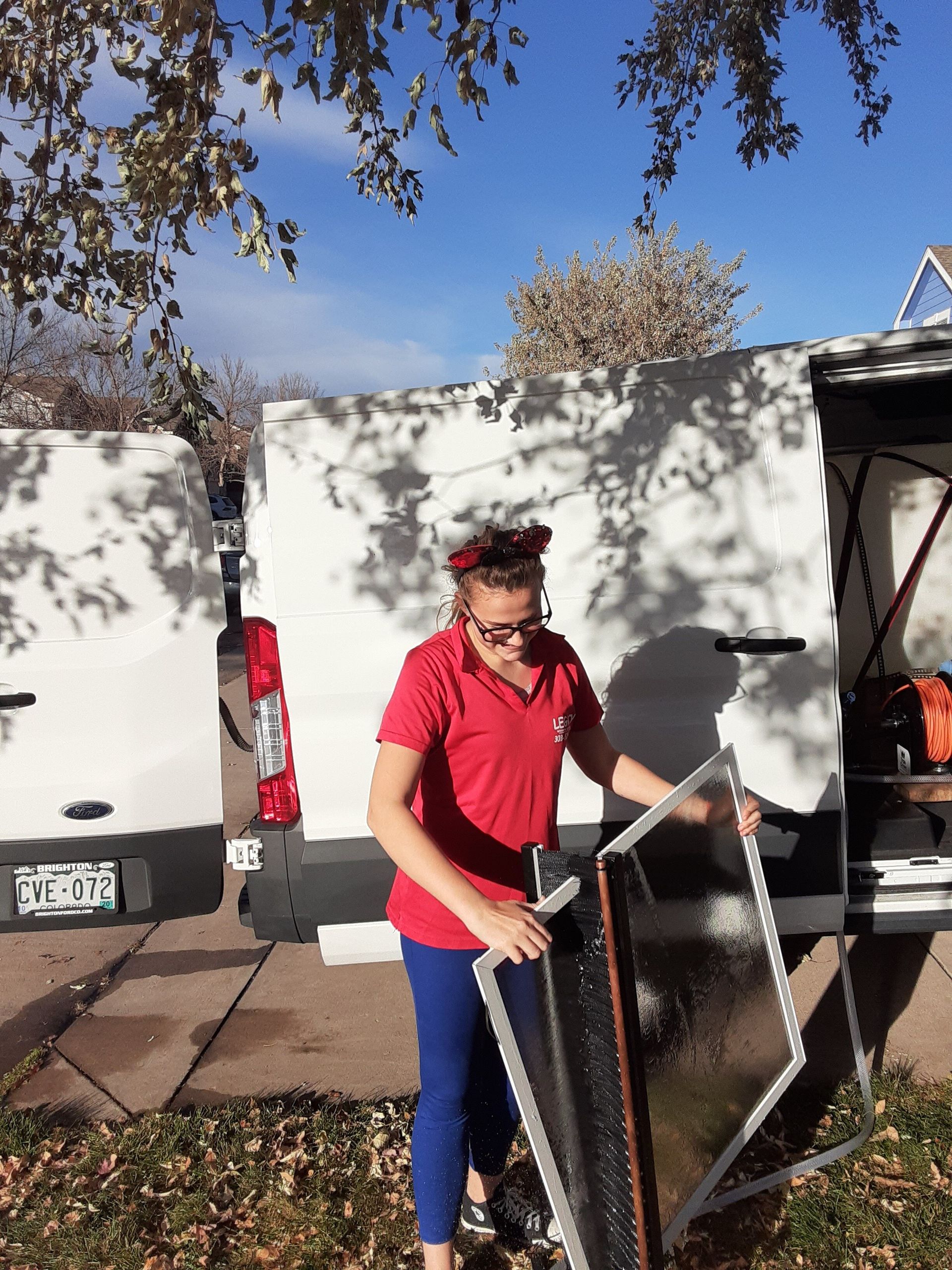 A woman in a red shirt is holding a screen in front of a white van.