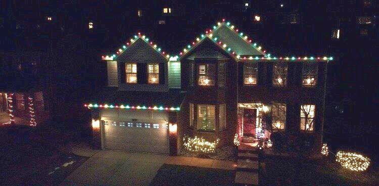 A house with christmas lights on the roof and a tree in front of it
