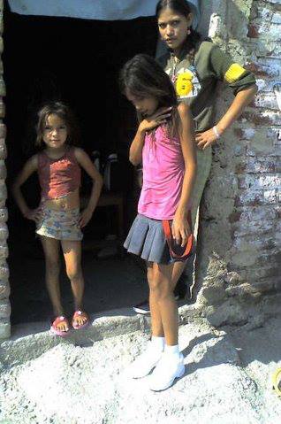 Three young girls are standing in front of a brick wall.