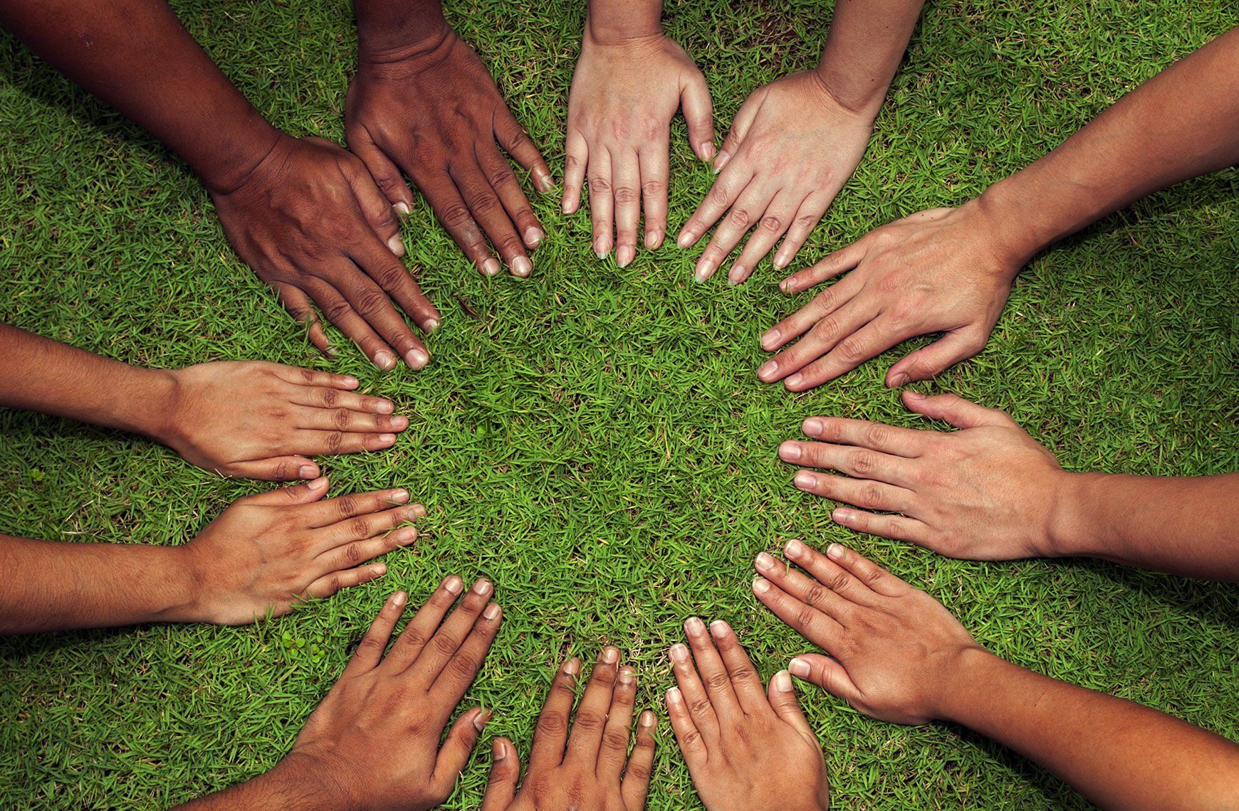 A group of people are putting their hands together in a circle on the grass.