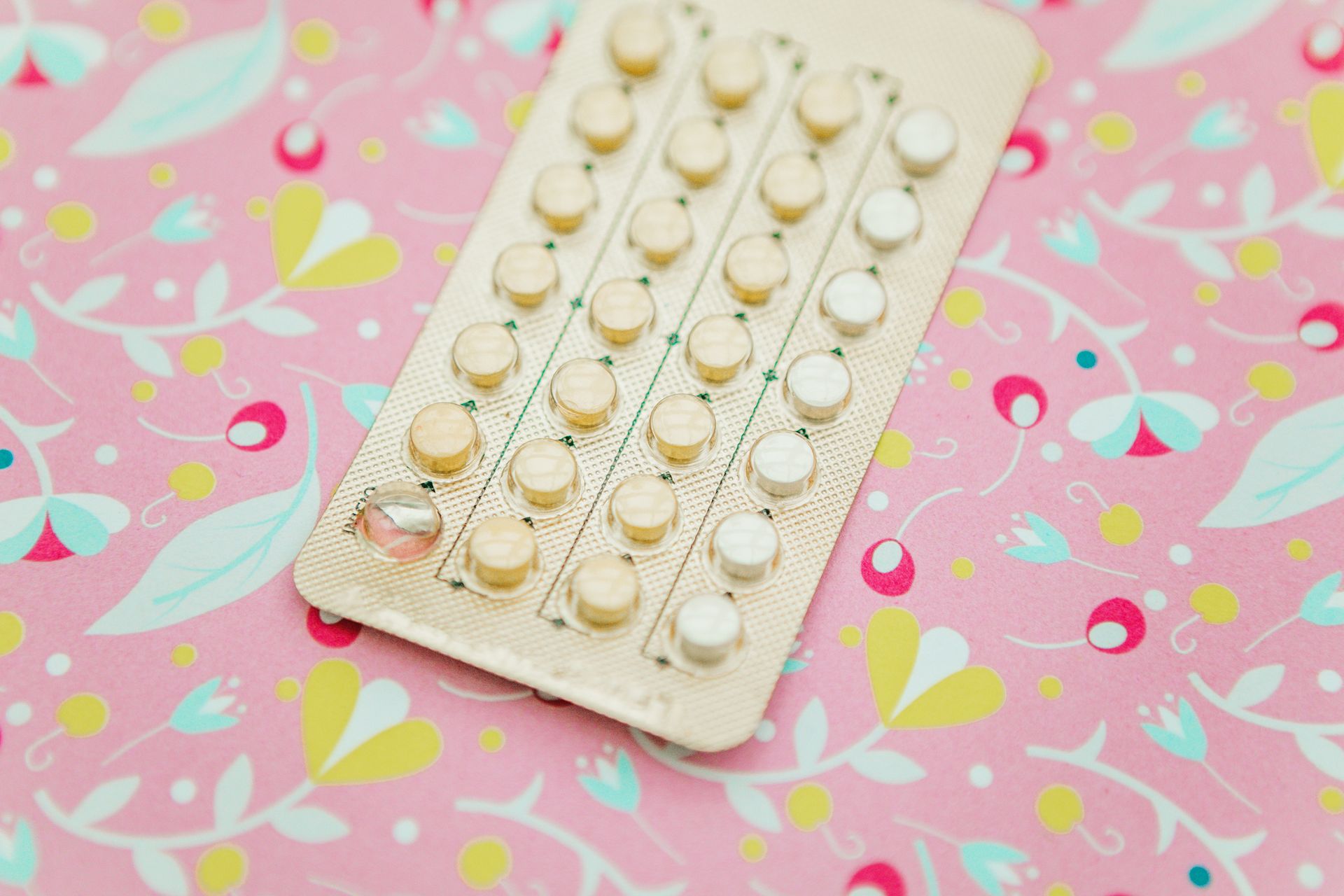 Confezione blister di pillole contraccettive su sfondo floreale rosa