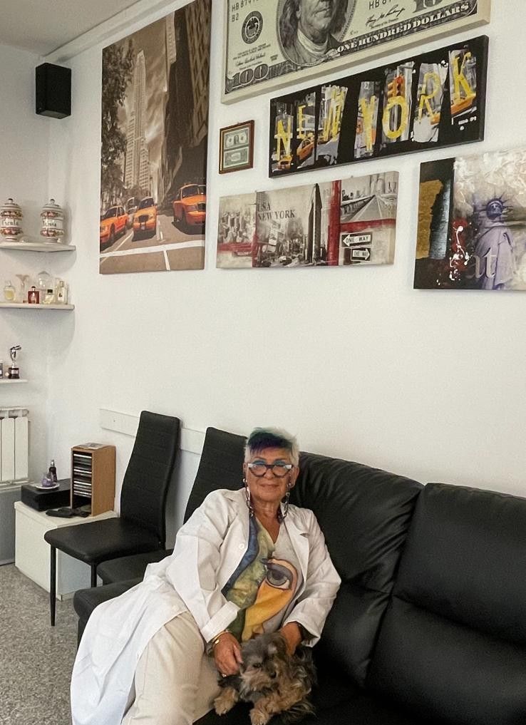 Una persona seduta su un divano nero con un cane, in una stanza decorata con quadri e mensole.