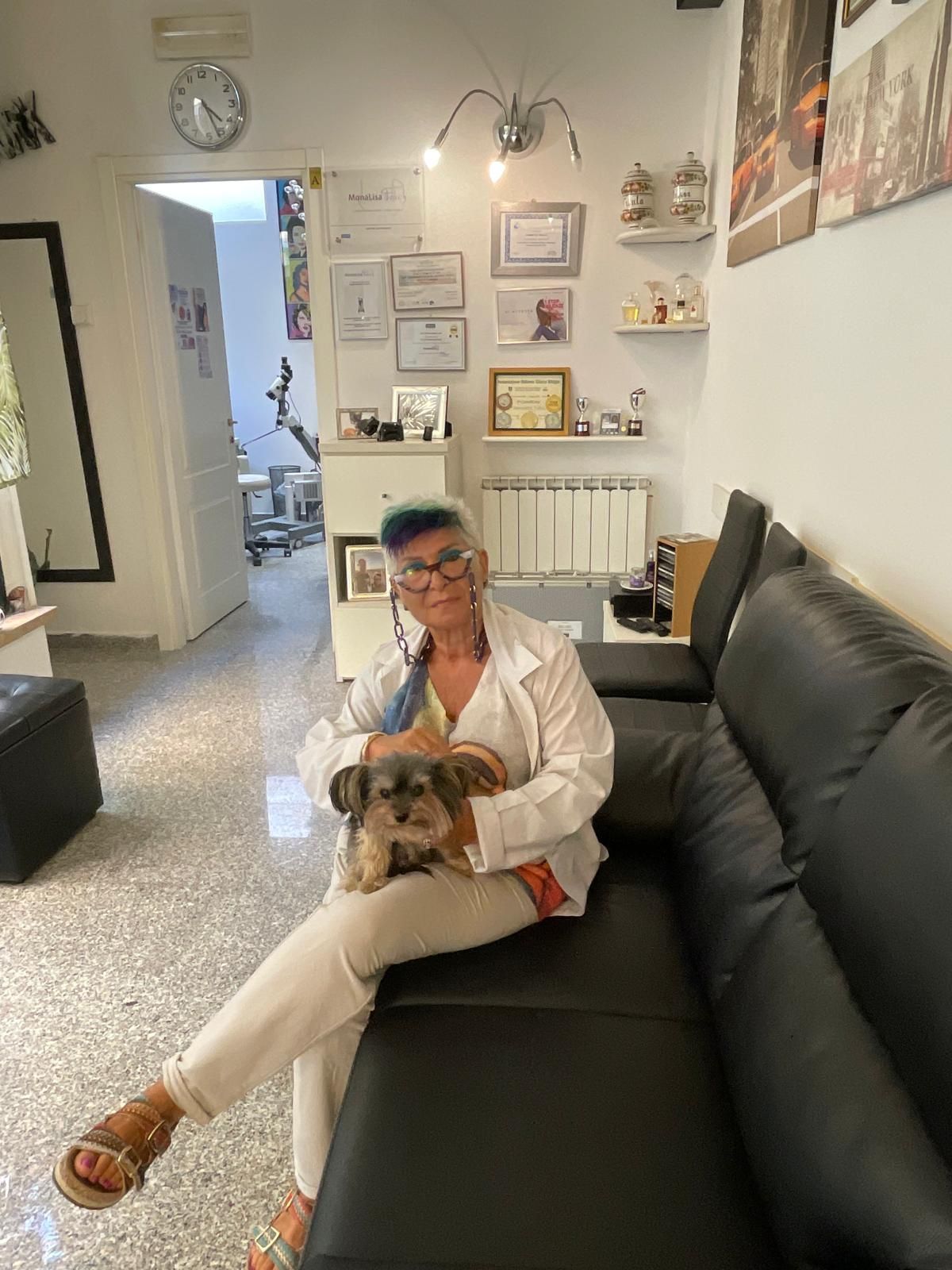 Una persona è seduta su un divano nero e tiene in braccio un cagnolino in una luminosa sala d'attesa