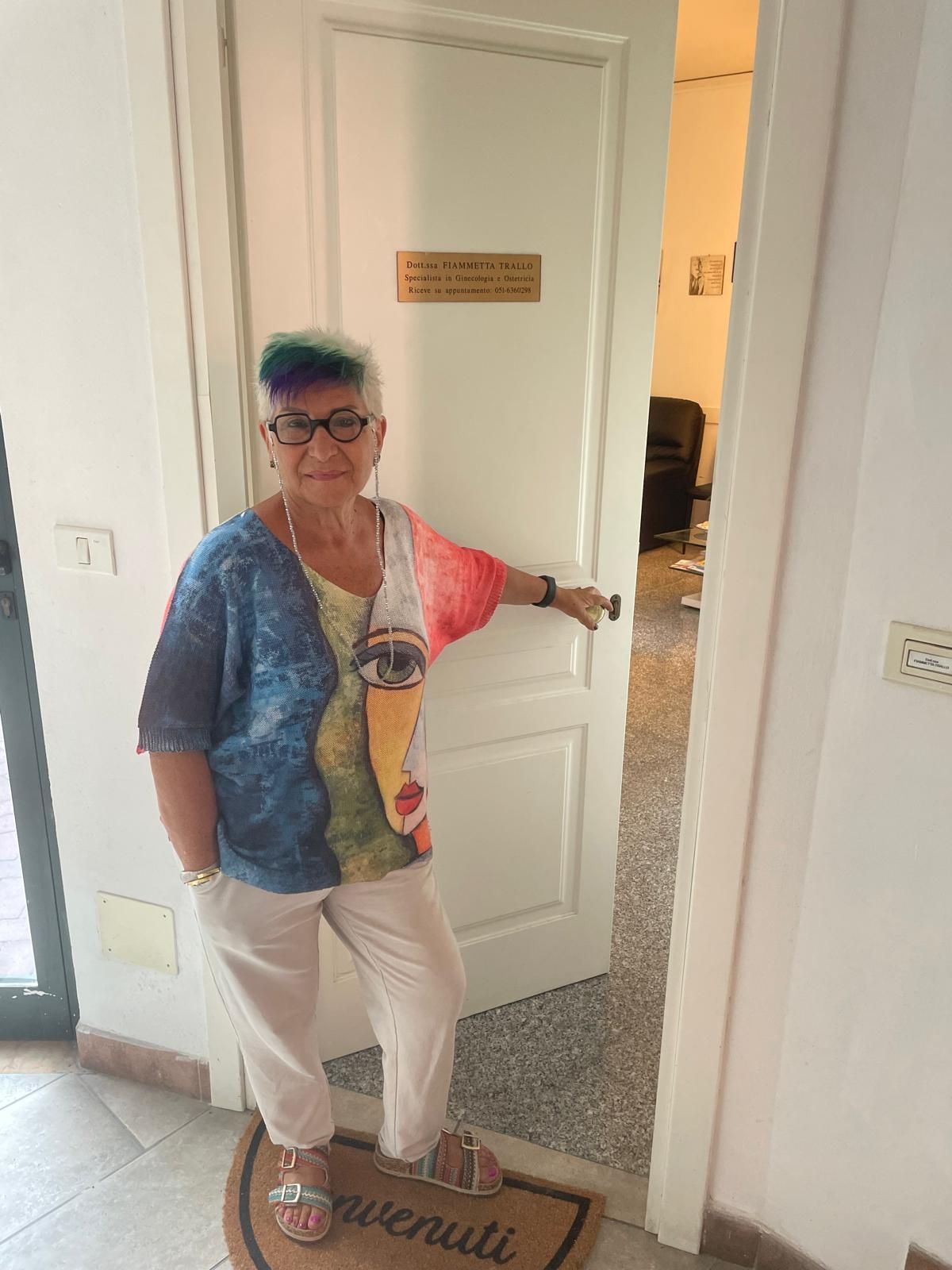 Una persona in piedi sulla soglia di una porta, che la tiene aperta in un corridoio luminoso.