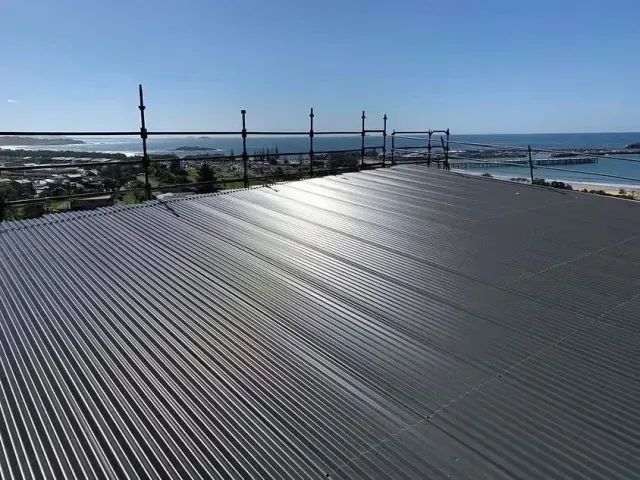 A aluminum roof with the sun reflecting on it and ocean in the background— Rhythm Roofing in Kempsey, NSW