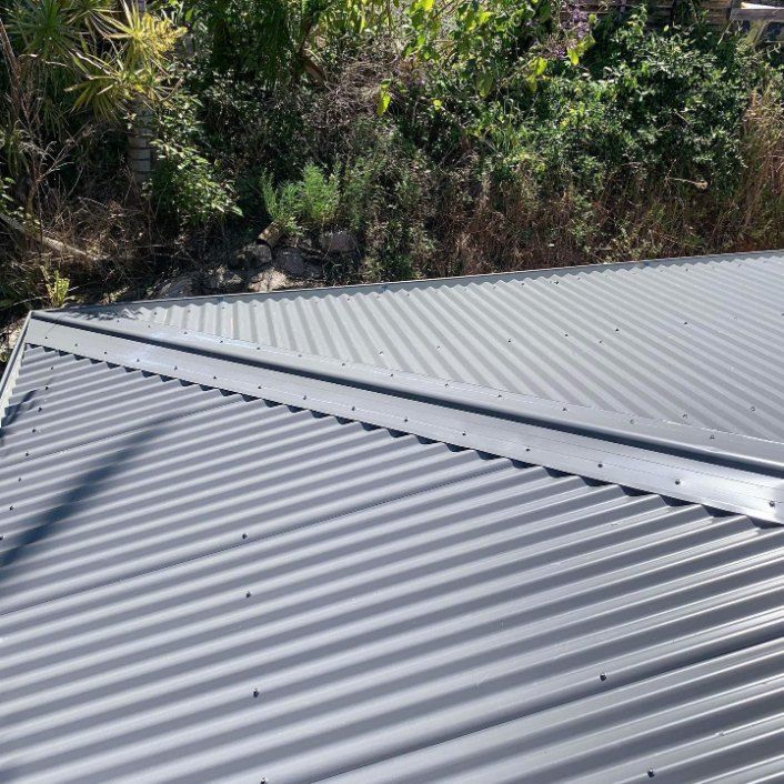 A Close Up of a Gray Corrugated Metal Roof With Trees in the Background — Rhythm Roofing in Nambucca Heads, NSW