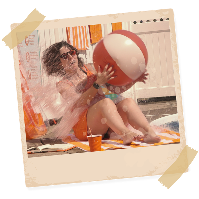 A woman is sitting by the pool holding a splashed by the water and hit with a beach ball