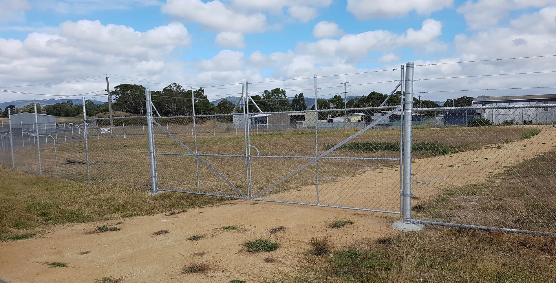 Chain-link fence around a dry field under a partly cloudy sky.