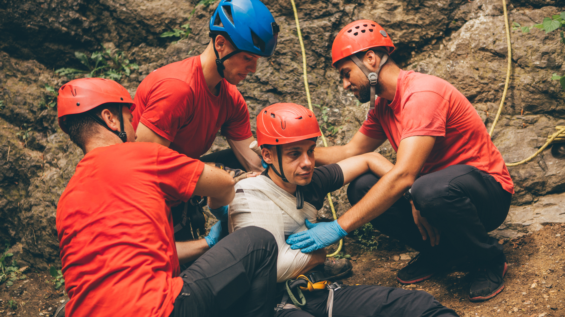 Rescuer in red uniform performing CPR on a manikin outdoors beside an open emergency kit
