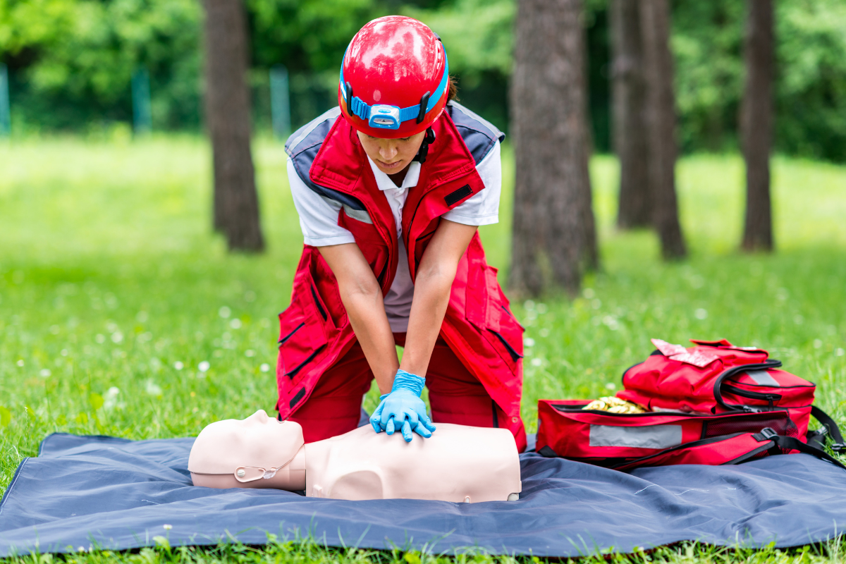 A man is practicing a heart attack on a mannequin in a park.