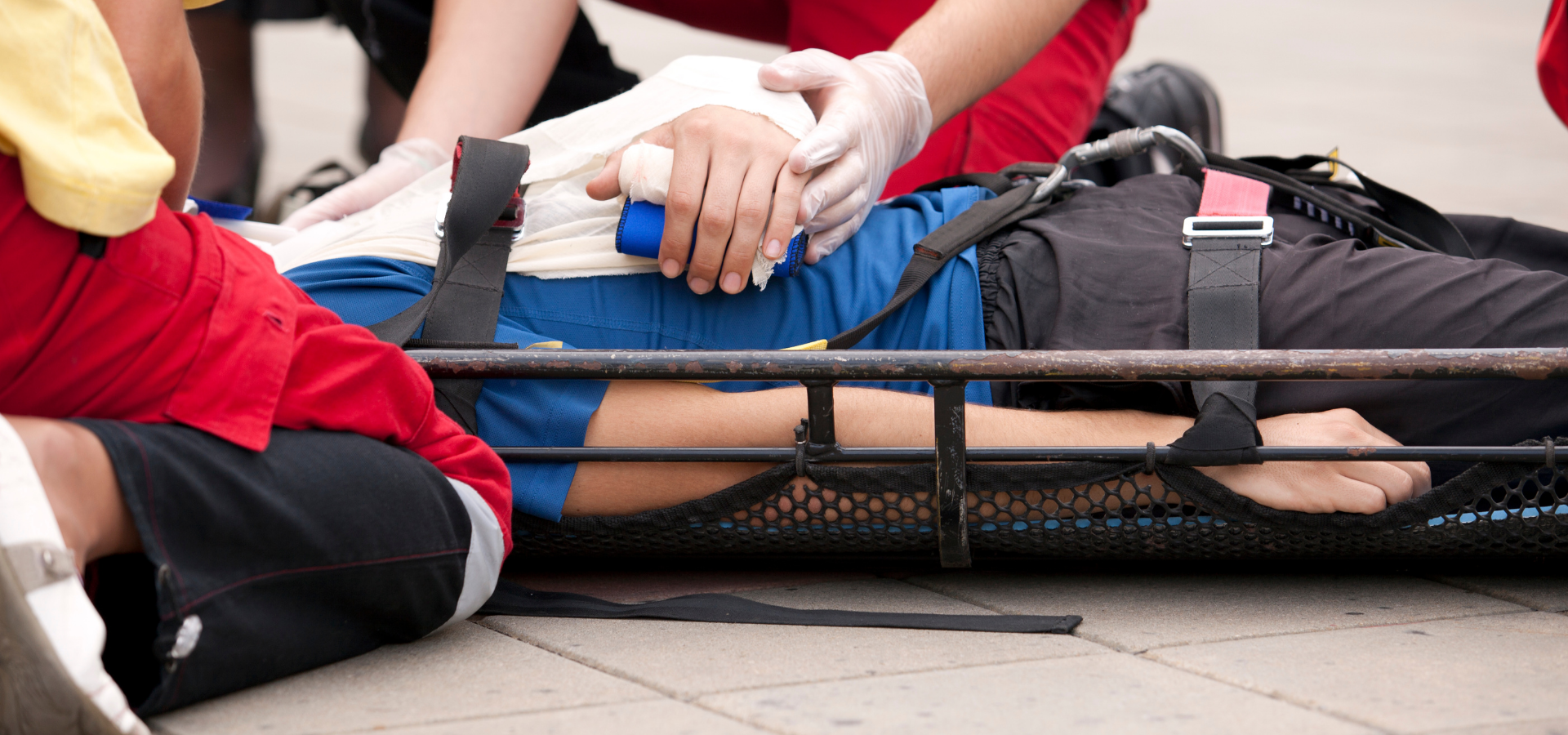 Person lying on a stretcher while responders secure them with straps and provide first aid