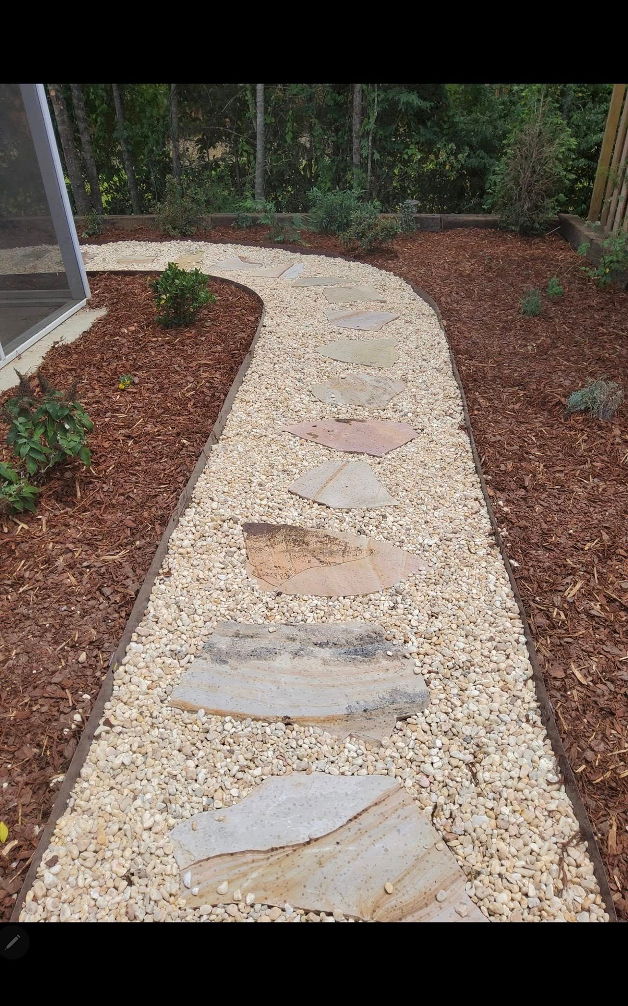 Curved gravel garden path with flat stepping stones bordered by mulch and shrubs
