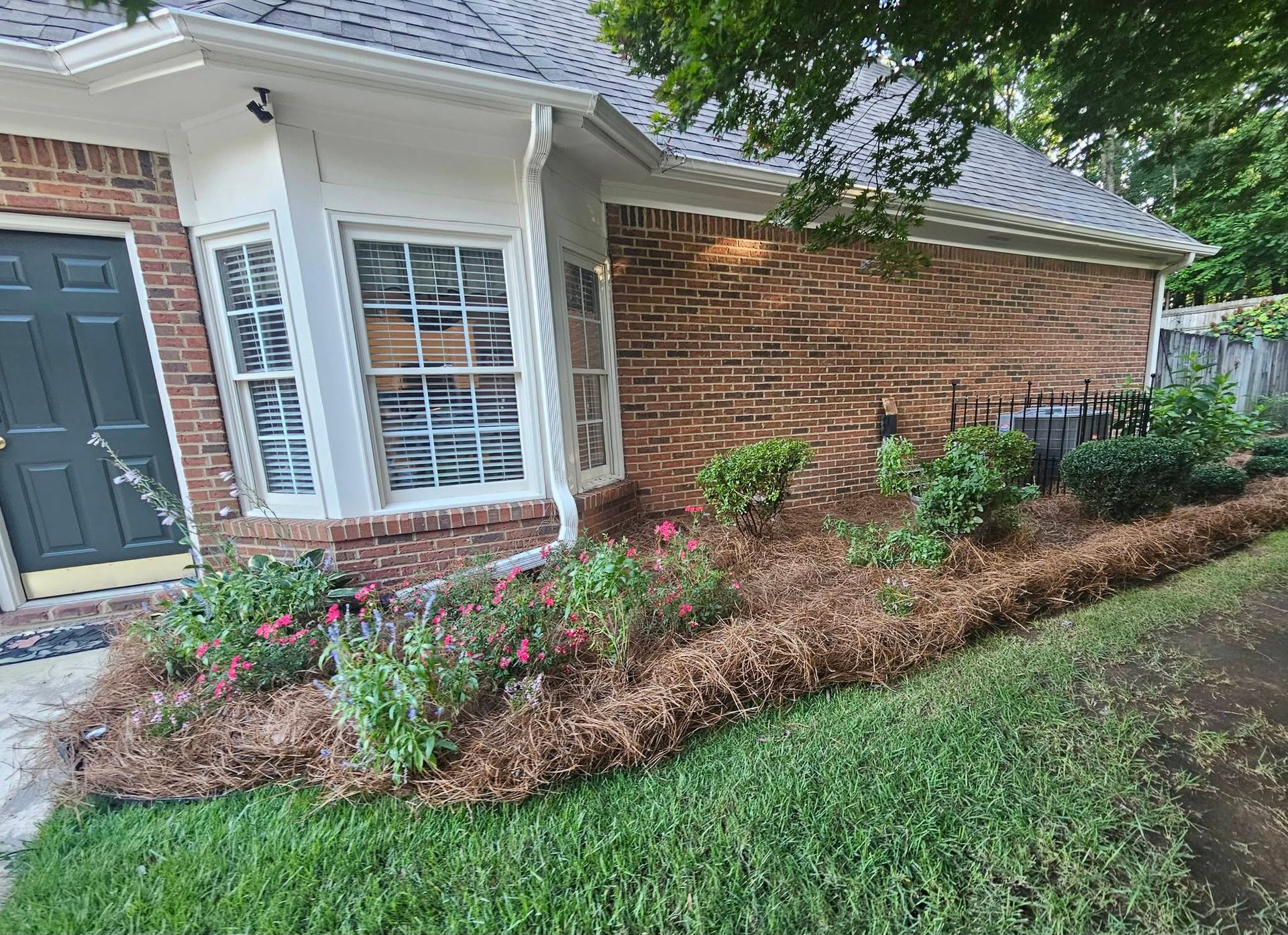 Brick house front entrance with white trim, gray door, and landscaped flower bed by the lawn