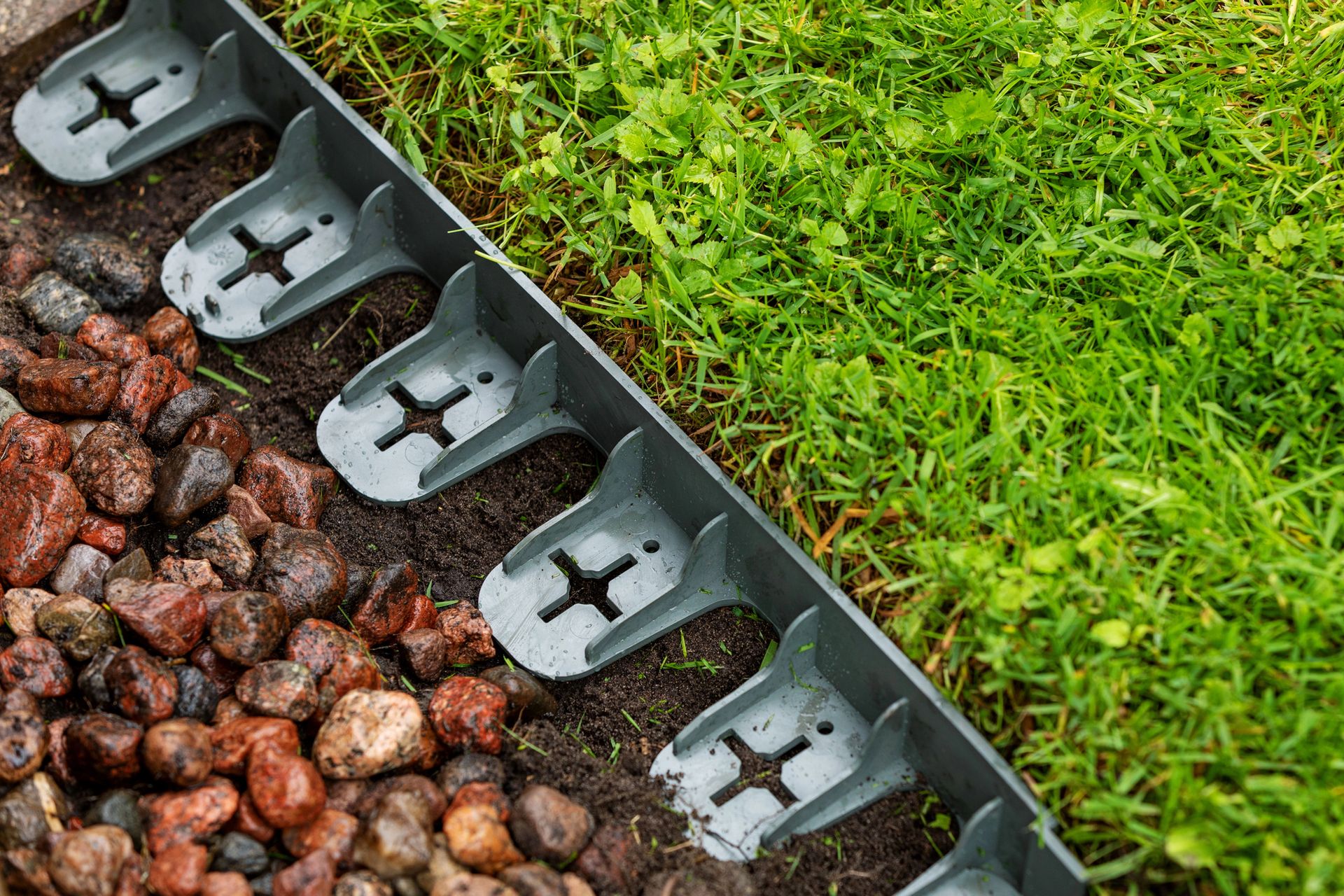 Black garden edging holds red rocks beside a green lawn