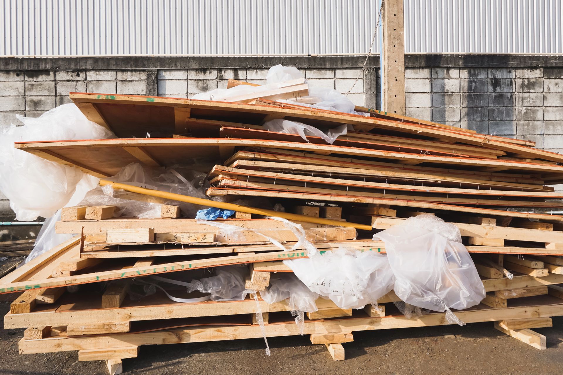 Stacked wooden pallets and broken boards piled outdoors beside a concrete wall.