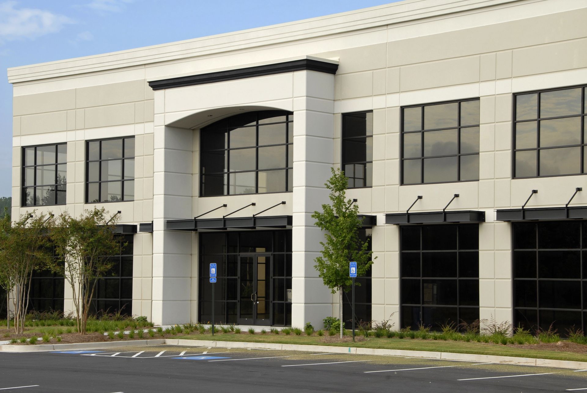 Modern two-story office building with light gray facade, large windows, and a central entrance.