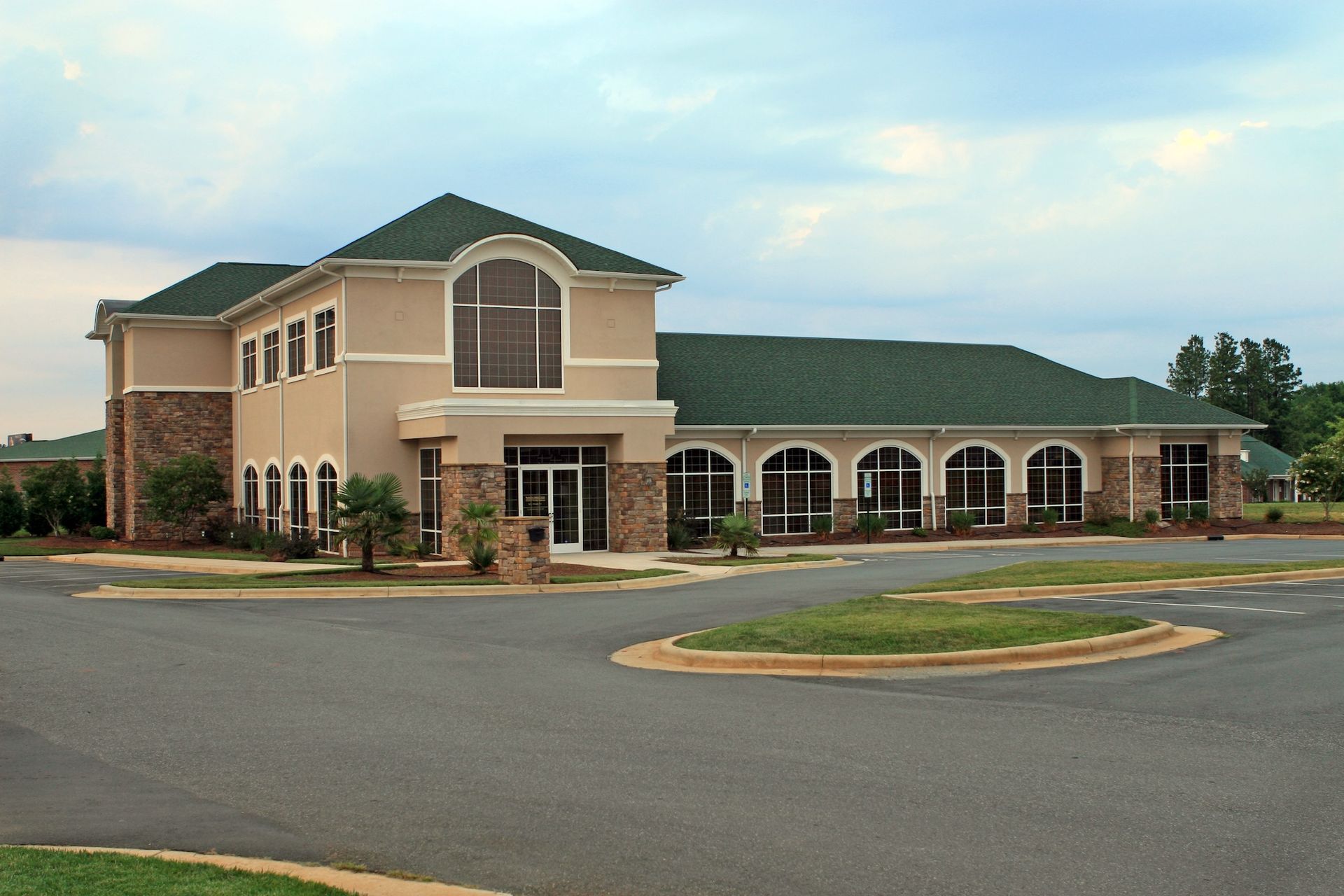 Brick office building with arched windows, green roof, and empty parking lot at dusk