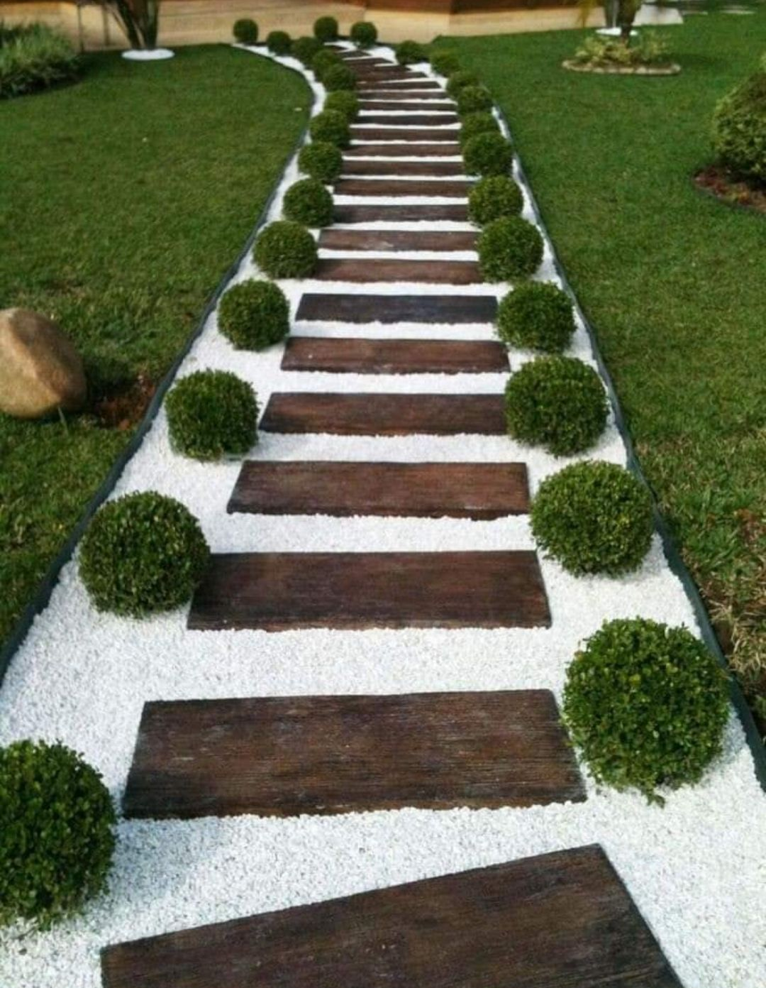 Stone and wood stepping path through green lawn, lined with round shrubs