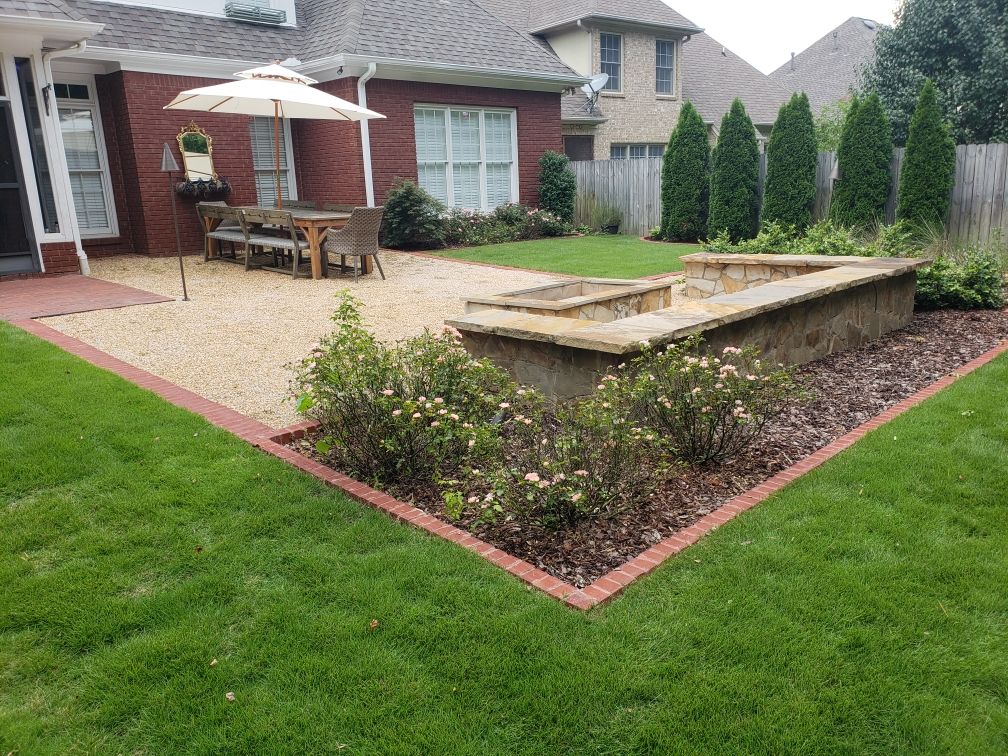 Backyard patio with stone seating wall, umbrella table, and landscaped garden beds beside a brick house