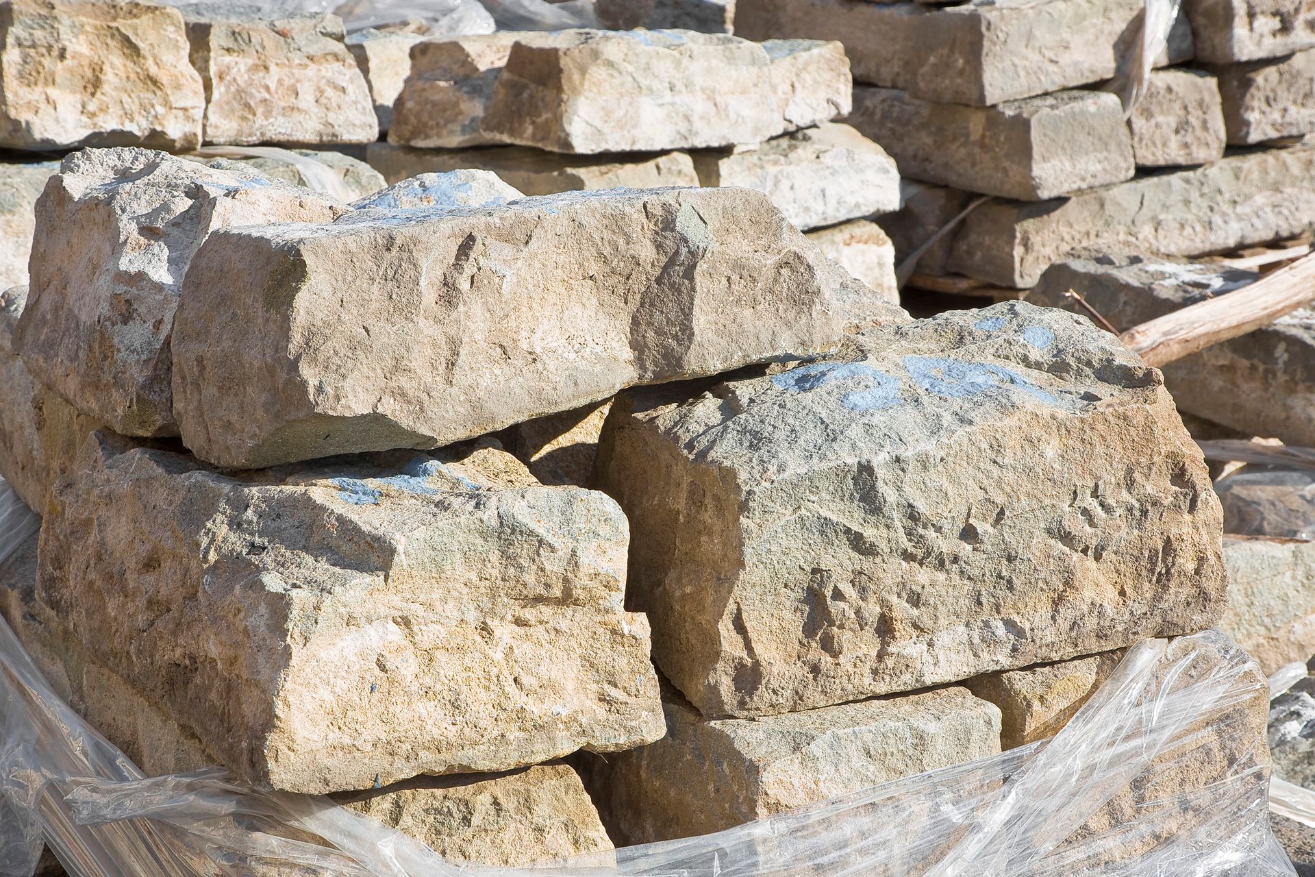 Stacked rough beige stone blocks piled outdoors against a rocky background.