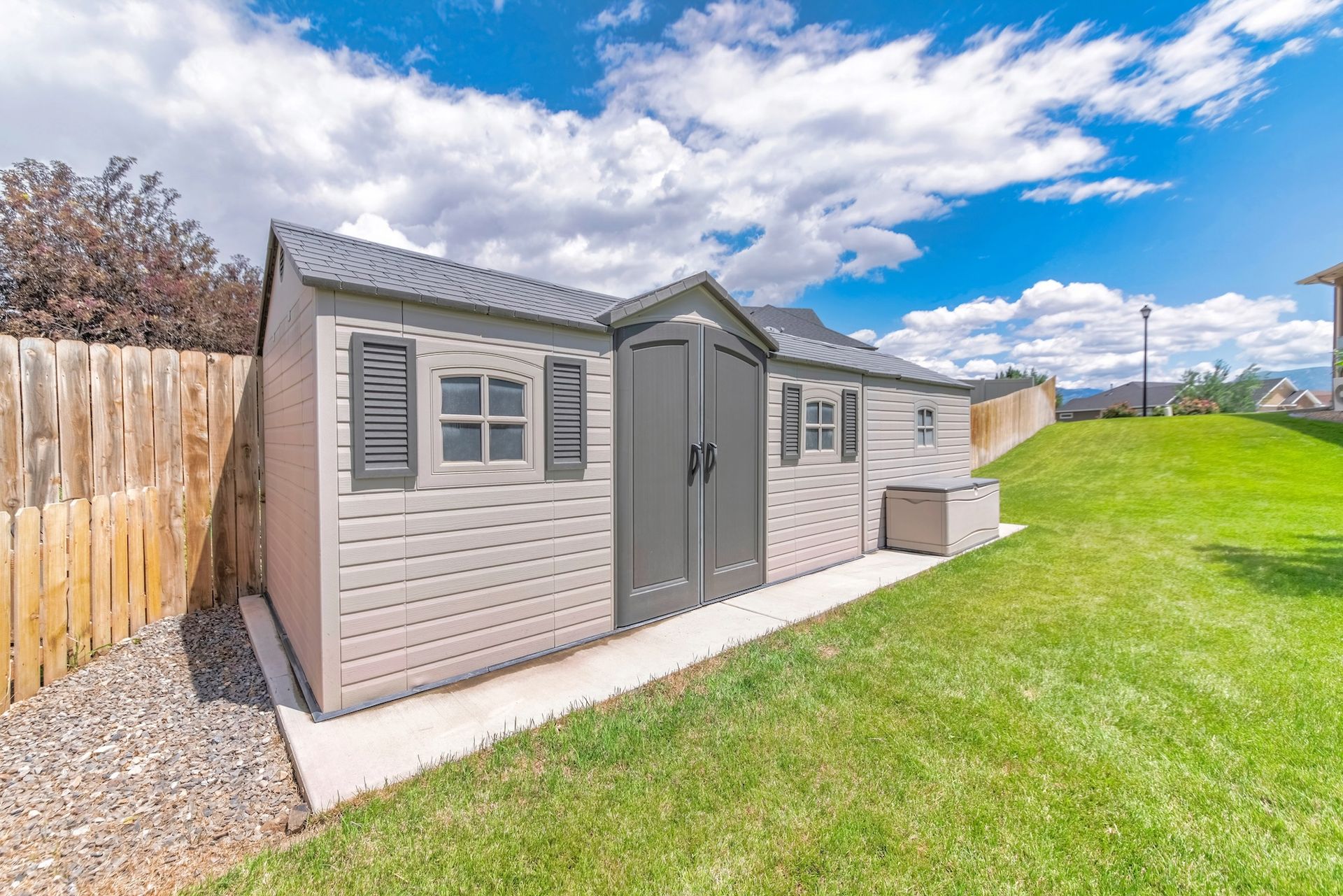 Gray outdoor storage shed beside a wooden fence, set along a grassy yard under a blue sky