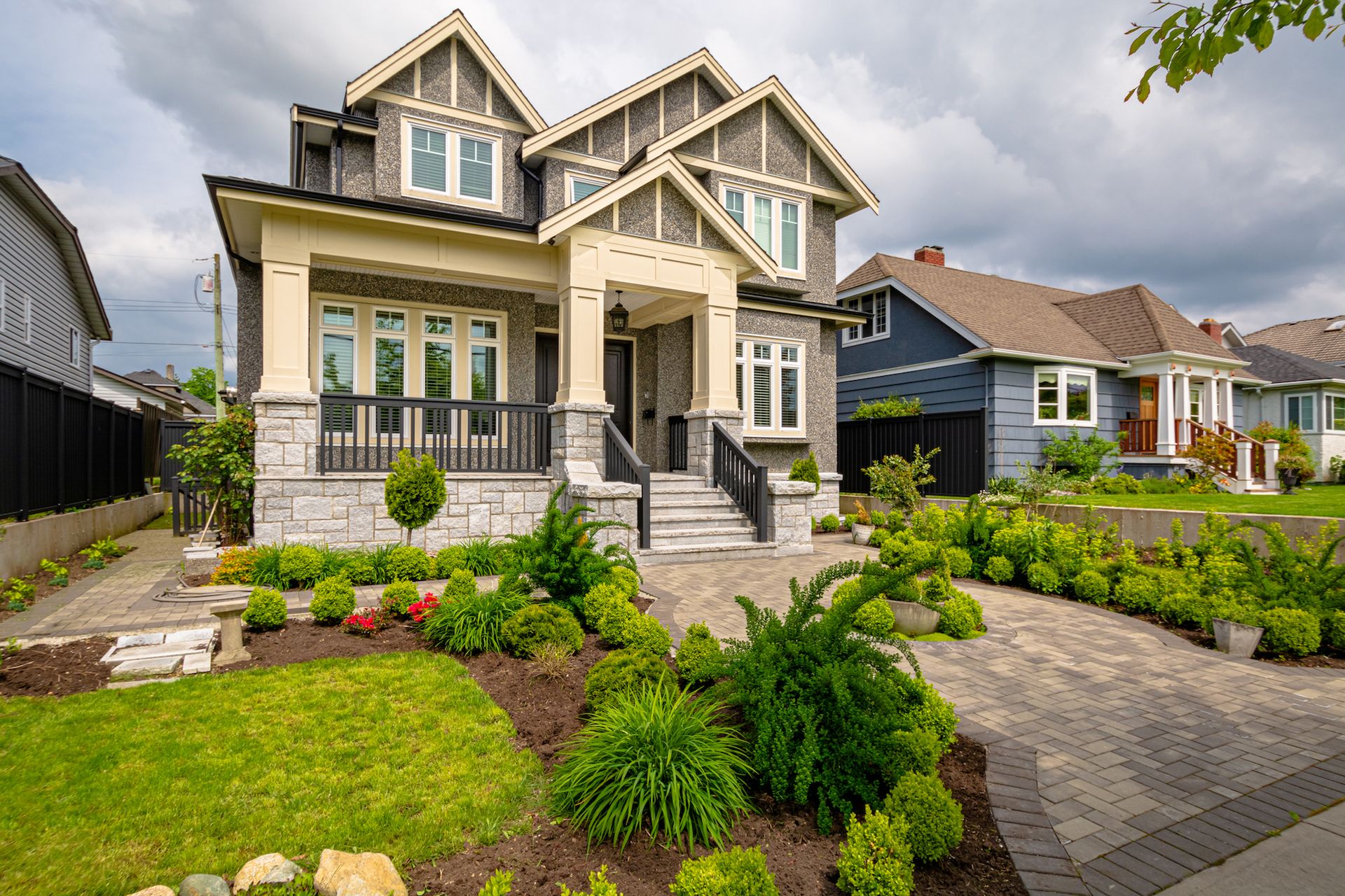 Large beige two-story house with a landscaped front yard and stone walkway under a cloudy sky
