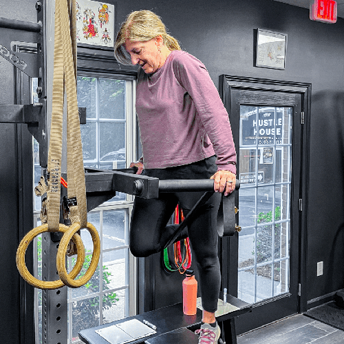Woman using parallel bars in a gym, balancing on one leg while holding the rails.