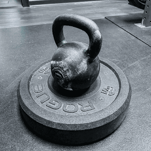 A black kettlebell resting on a weight plate at Hustle House in Woodstock, GA.