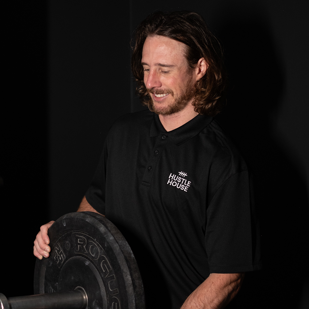 Man in a black shirt holding a weight plate against a dark background