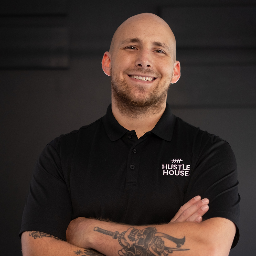 Smiling man in black polo with arms crossed against a dark studio background
