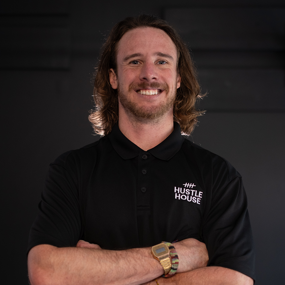 Smiling person in a black polo with arms crossed against a dark background