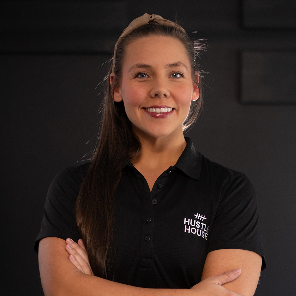 Portrait of a smiling person in a black Host House polo shirt with arms crossed