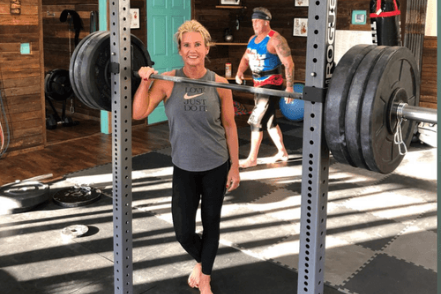 A woman is holding a barbell over her head in a gym.