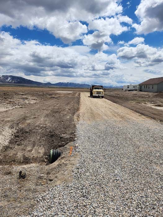 Gravel road construction in a wide open field. Dump truck driving on fresh gravel, under a cloudy sky.