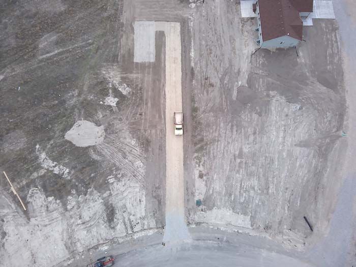 Aerial view of a light-colored truck on a long gravel driveway leading to a house with a brown roof.