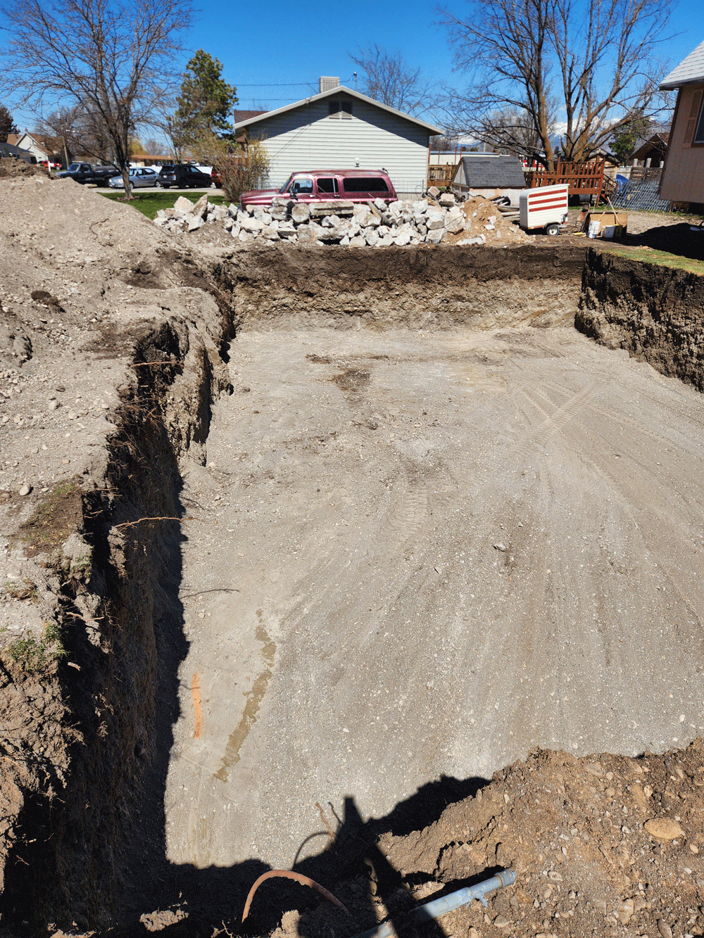 Deep concrete excavation pit in a residential yard, with dirt mounds and a house in the background