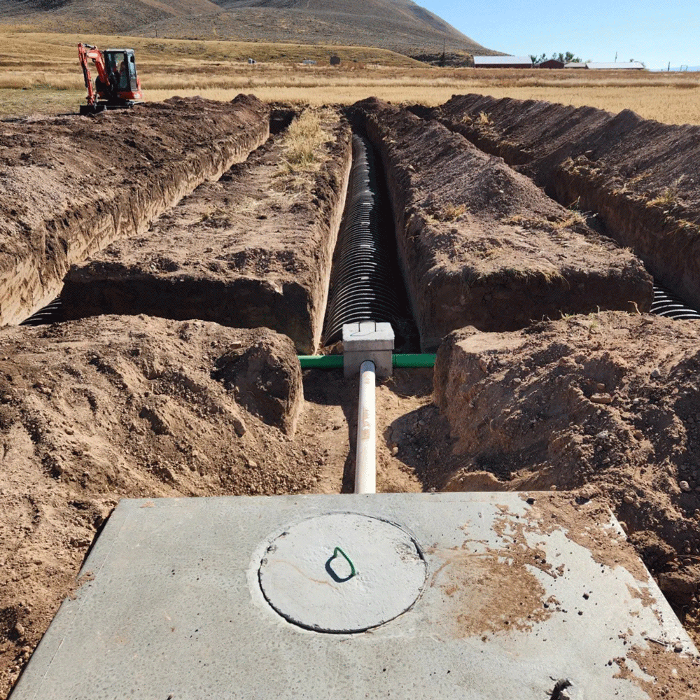Trenched pipe installation in a dry dirt field with an excavator in the distance