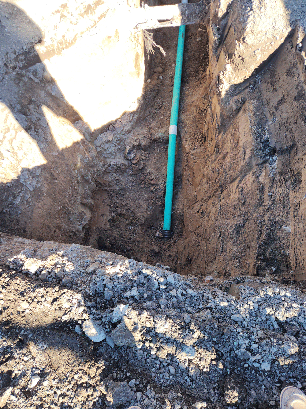 A dirt excavation pit with a green measuring rod standing upright against the wall.