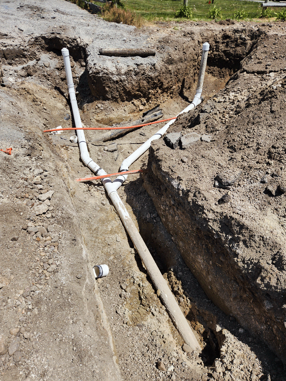 Trenched ground with exposed white PVC pipes and orange tape at a construction site