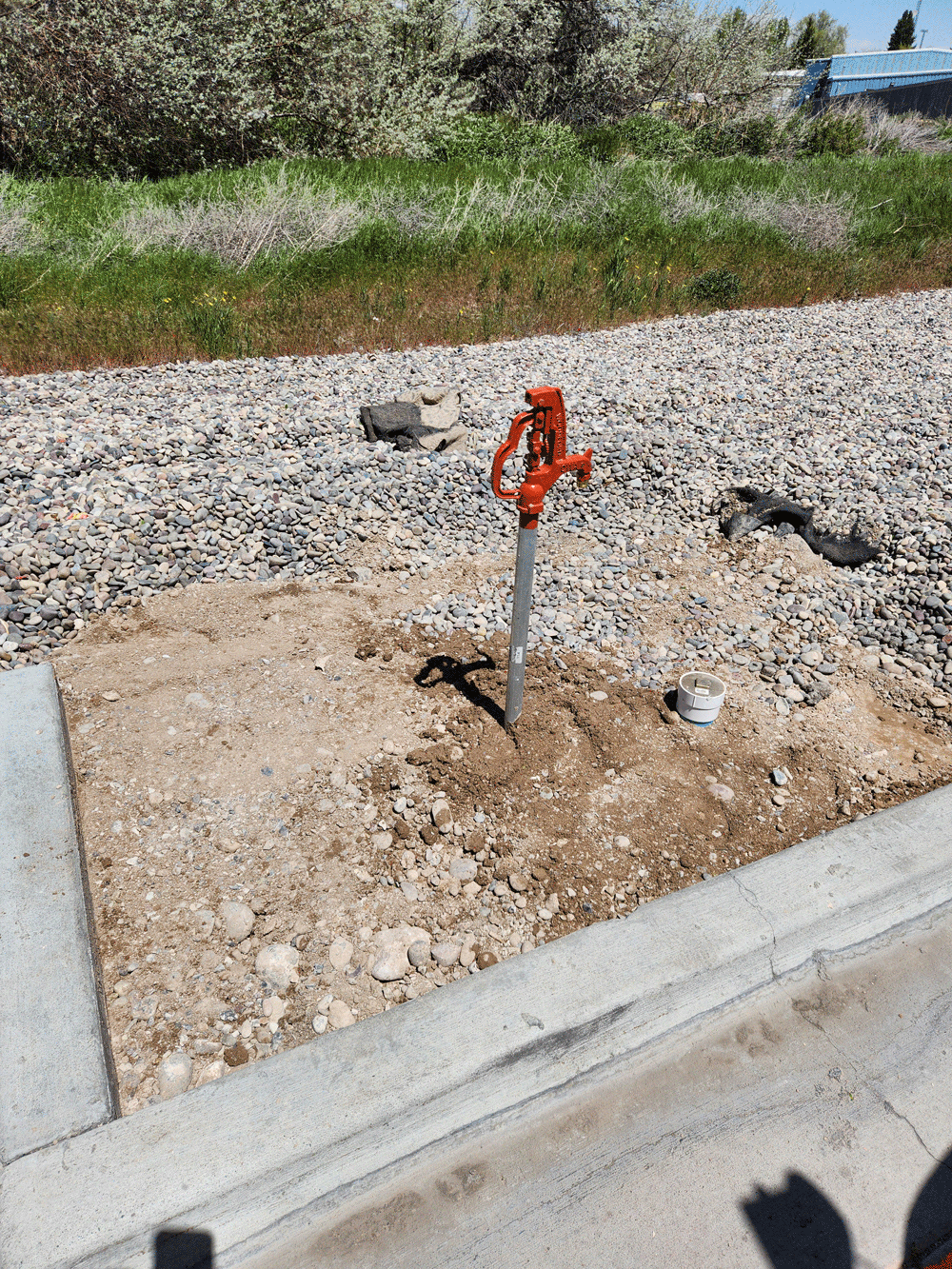 Orange irrigation valve in a gravel landscaping area beside a concrete curb.