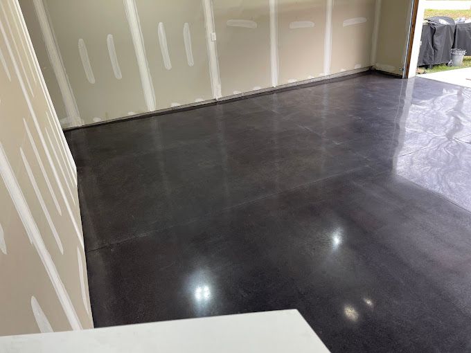 Dark polished concrete floor inside a room, with drywall walls.