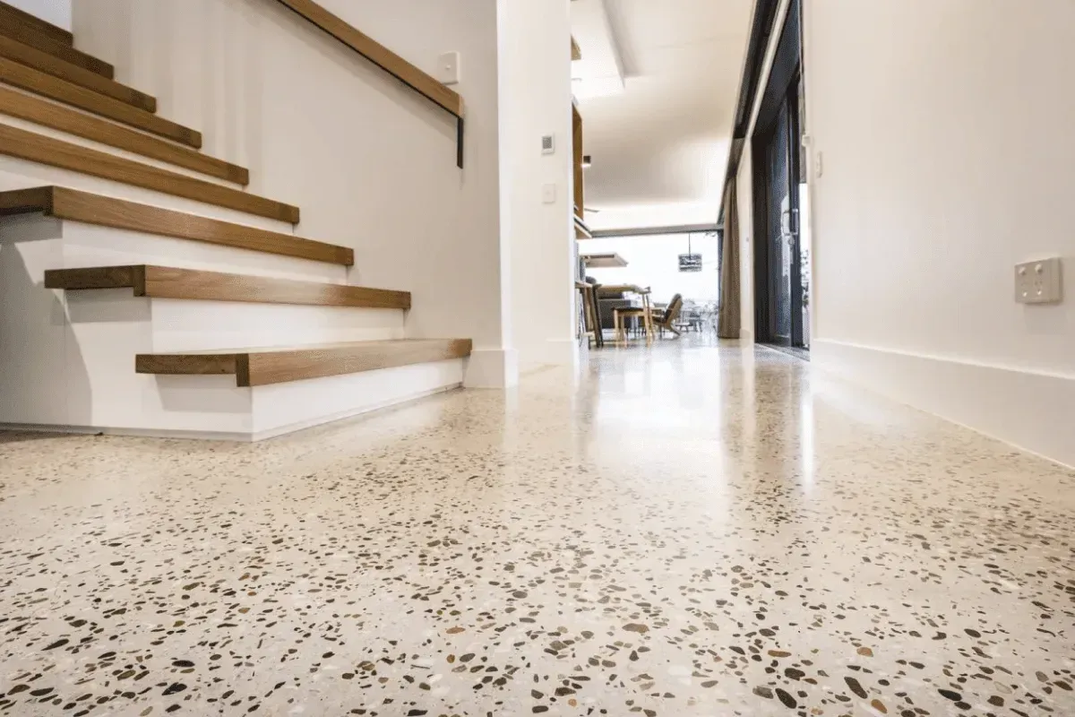 Polished concrete floor with stairs leading up. White walls, wooden stairs and railing.
